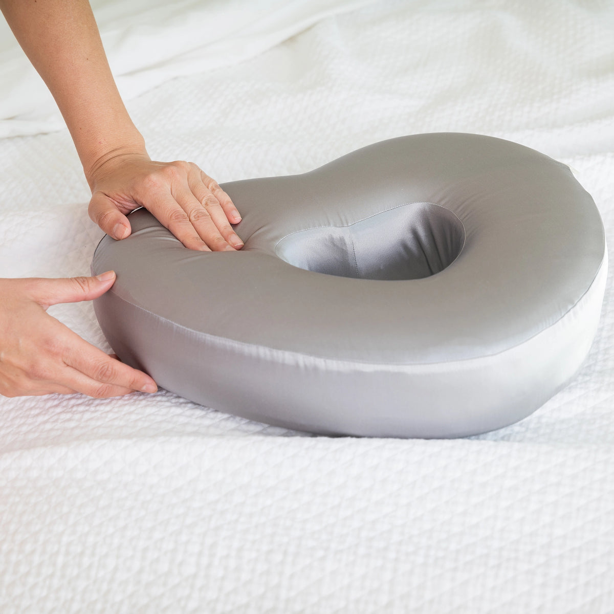 Charcoal Longevity Pillow being held by a person on a white bed